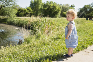 Seitenansicht eines süßen Jungen, der eine Latzhose trägt, während er am See im Park steht - CAVF51784