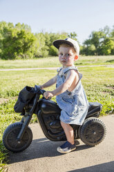 Porträt eines süßen Jungen auf einem Spielzeugmotorrad im Park - CAVF51786