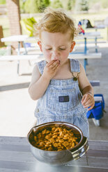 Cute boy wearing bib overalls while eating crackers from bowl - CAVF51789