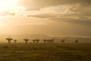 Satellitenschüssel auf einem Feld vor bewölktem Himmel bei Sonnenuntergang - CAVF51793