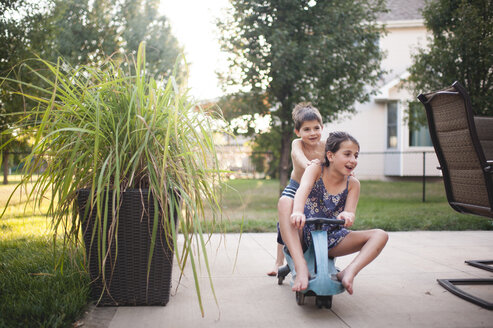 Playful siblings playing on moped scooter at backyard - CAVF51836