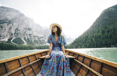 Frau schaut weg, während sie in einem Ruderboot auf einem See vor den Bergen sitzt - CAVF51853