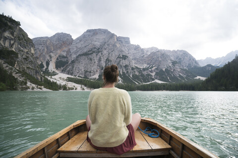 Rückansicht einer Frau, die in einem Boot auf einem Fluss inmitten eines Berges vor dem Himmel sitzt, lizenzfreies Stockfoto