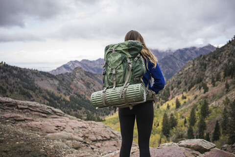 Rückansicht einer Wanderin mit Rucksack auf einem Berg vor bewölktem Himmel, lizenzfreies Stockfoto