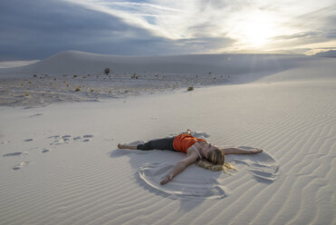 Woman lying on sand against cloudy sky - CAVF51863