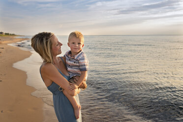 Porträt eines süßen Sohnes, der von seiner Mutter am Strand bei Sonnenuntergang getragen wird - CAVF51872