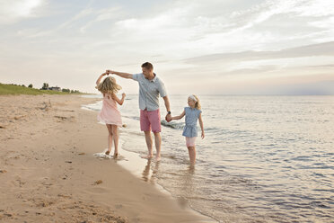 Father playing with daughters on shore at beach - CAVF51873