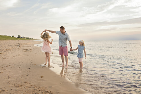 Vater spielt mit Töchtern am Ufer des Strandes - CAVF51873