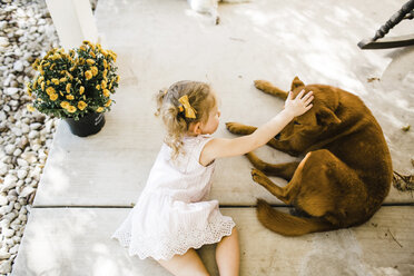 Hohe Winkel Ansicht von Mädchen streicheln Hund, während auf der Veranda liegen - CAVF51876