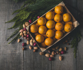 Hohe Winkelansicht von Orangen in einer Kiste mit verschiedenen Trockenfrüchten und Pflanzen auf einem Holztisch - CAVF51892