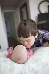 Bruder küsst kleines Mädchen, das zu Hause auf dem Bett liegt - CAVF51919