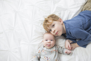 Overhead portrait of cute siblings lying on bed at home - CAVF51920