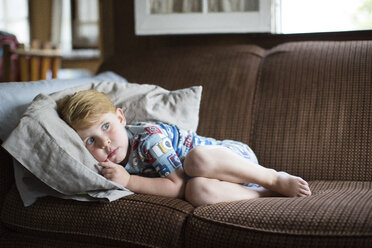 Verängstigter Junge in voller Länge auf dem Sofa zu Hause liegend - CAVF51925
