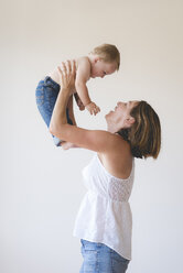 Side view of playful mother lifting shirtless son against white background - CAVF51932