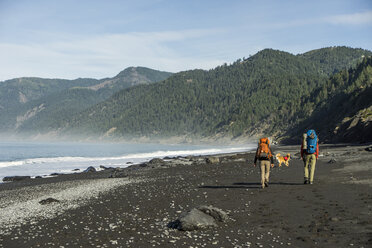 Rückansicht von Wanderern mit Rucksäcken und Hund am Strand gegen Berge und Himmel - CAVF51953