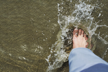 Low section of man stamping foot in water on shore - CAVF51963