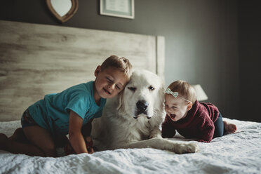 Geschwister spielen mit Great Pyrenees auf dem Bett zu Hause - CAVF51964