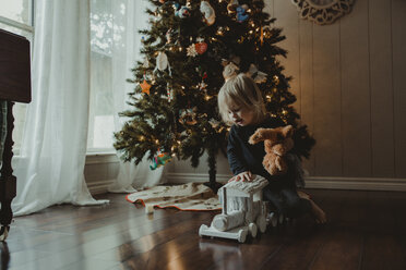 Mädchen spielt mit Spielzeug gegen Weihnachtsbaum zu Hause - CAVF51966