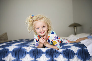 Porträt eines fröhlichen Mädchens, das auf einem Bett an der Wand liegt - CAVF51969
