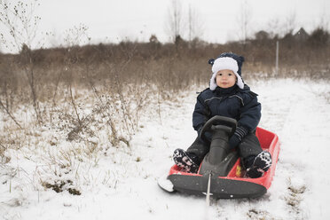 Porträt eines niedlichen kleinen Jungen in voller Länge auf einem Schlitten im Schnee sitzend - CAVF51970
