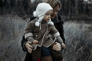 Mutter mit Tochter auf einer Wiese im Wald sitzend im Winter - CAVF51978