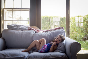 Portrait of girl lying on sofa by window at home - CAVF51994