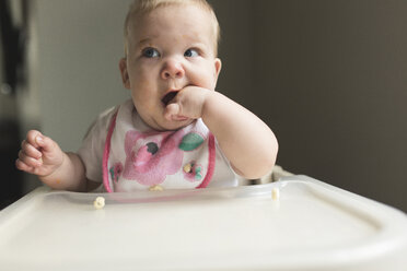 Cute baby girl with finger in mouth sitting on high chair at home - CAVF52007