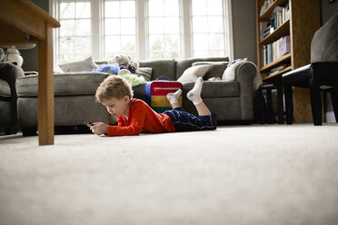 Junge in voller Länge bei der Benutzung eines Smartphones, während er zu Hause auf dem Teppich liegt - CAVF52012