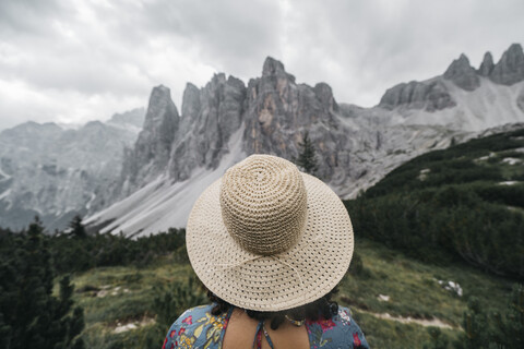 Rückansicht einer Wanderin mit Hut auf einem Berg vor bewölktem Himmel, lizenzfreies Stockfoto