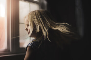 Seitenansicht eines Mädchens, das zu Hause am Fenster steht - CAVF52064