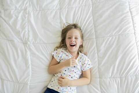 Overhead-Porträt eines fröhlichen Mädchens auf dem Bett liegend, lizenzfreies Stockfoto