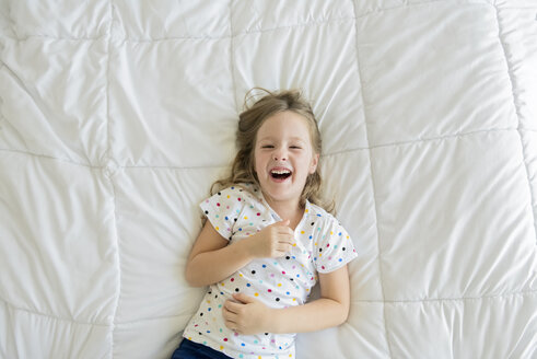 Overhead-Porträt eines fröhlichen Mädchens auf dem Bett liegend - CAVF52081