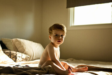 Porträt eines süßen Jungen ohne Hemd, der zu Hause auf dem Bett sitzt - CAVF52084