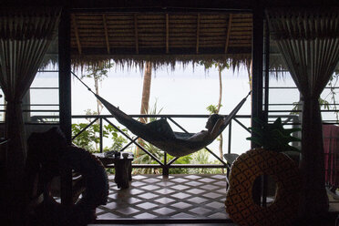 Side view of woman relaxing on hammock in cottage against sea - CAVF52093