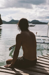 Thoughtful shirtless man sitting on jetty over sea - CAVF52096
