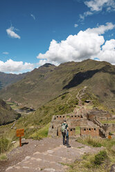 Rear view of hiker looking at old ruins while standing on mountain against sky at Pisac - CAVF52109