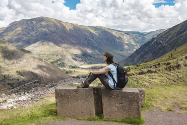 Seitenansicht einer Frau mit Rucksack auf einem Berg sitzend gegen einen bewölkten Himmel bei Pisac - CAVF52110