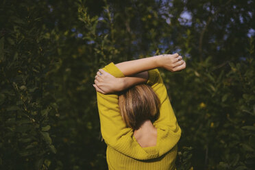 Rear view of woman with arms raised while standing by plants in forest - CAVF52122