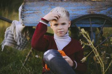 Porträt eines Jungen, der sein Haar berührt, während er gegen einen Wagen auf einem Feld sitzt - CAVF52130