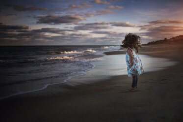 Playful girl jumping at beach against cloudy sky - CAVF52135