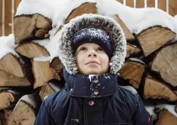 Junge, der im Winter an einem Baumstamm steht und nach oben schaut - CAVF52155