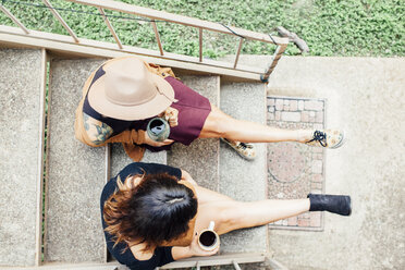 Blick von oben auf Freundinnen, die auf einer Treppe sitzend Kaffee trinken - CAVF52212