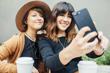 Lächelnde Freundinnen machen ein Selfie, während sie am Tisch sitzen - CAVF52218