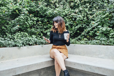 Woman using phone while sitting on bench at park - CAVF52222