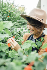 Smiling woman looking at flowers on plants - CAVF52223