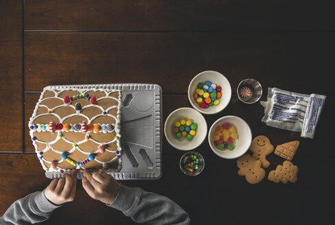 Cropped hands of boy making gingerbread house on wooden table during Christmas at home - CAVF52231