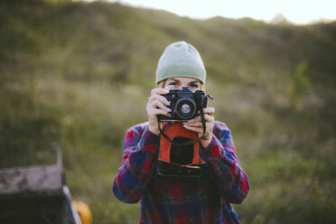 Junge Frau beim Fotografieren mit Kamera auf einem Feld stehend - CAVF52246