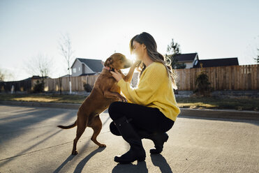 Frau spielt mit Hund und hockt auf der Straße gegen den klaren Himmel an einem sonnigen Tag - CAVF52281