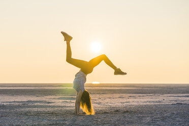 Side view of woman doing handstand at beach against clear sky during sunset - CAVF52314