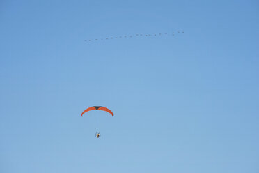 Low angle view of young man motor paragliding against clear blue sky - CAVF52329